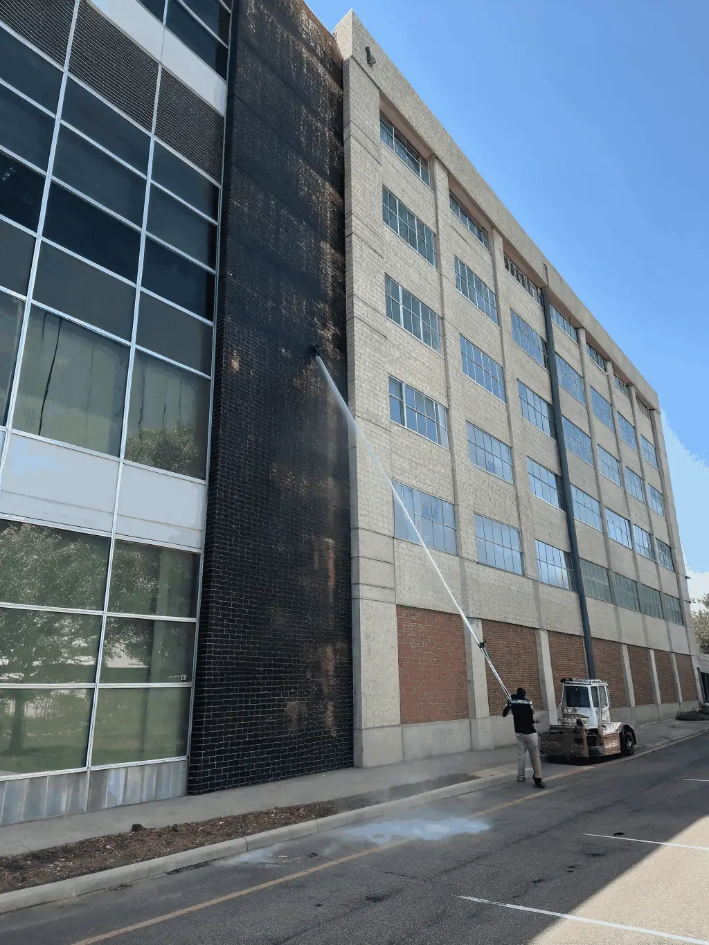 A commercial building exterior shown before and after washing, with one side dull and dirty and the other side bright and spotless, emphasizing the transformation.